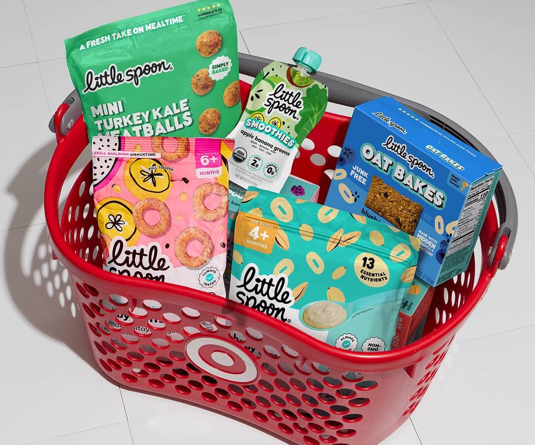 Red Target shopping basket filled with Little Spoon products, including Mini Turkey Kale Meatballs, a Smoothies pouch, Oat Bakes, and snacks.