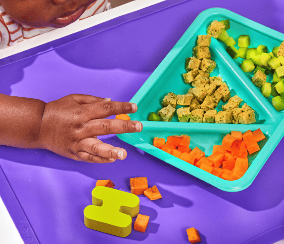 Baby fingers hovering over a tray of diced food suitable for early eaters and proper oral development.