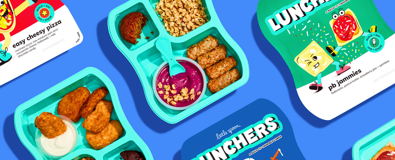 A group of Little Spoon Lunchers products including opened Chicken Dunkers with superfood chicken nuggets & yogurt ranch dip, and an opened Brunch Luncher with a Pitaya Bowl, granola, chicken maple mini sausages & a zucchini muffin. There are also some Easy Cheesy Pizza luncher & PB Jammies luncher boxes. The group of products is on a blue background.